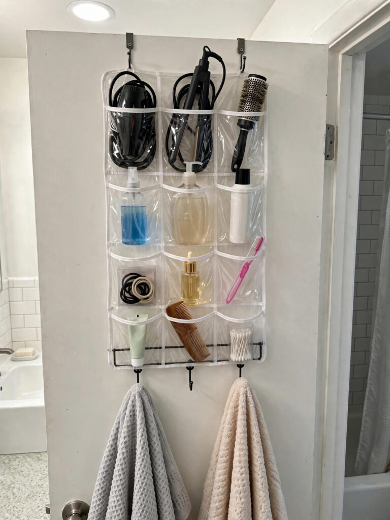 Over-the-door clear pocket organizer with hair tools and toiletries plus towel hooks on a bathroom door